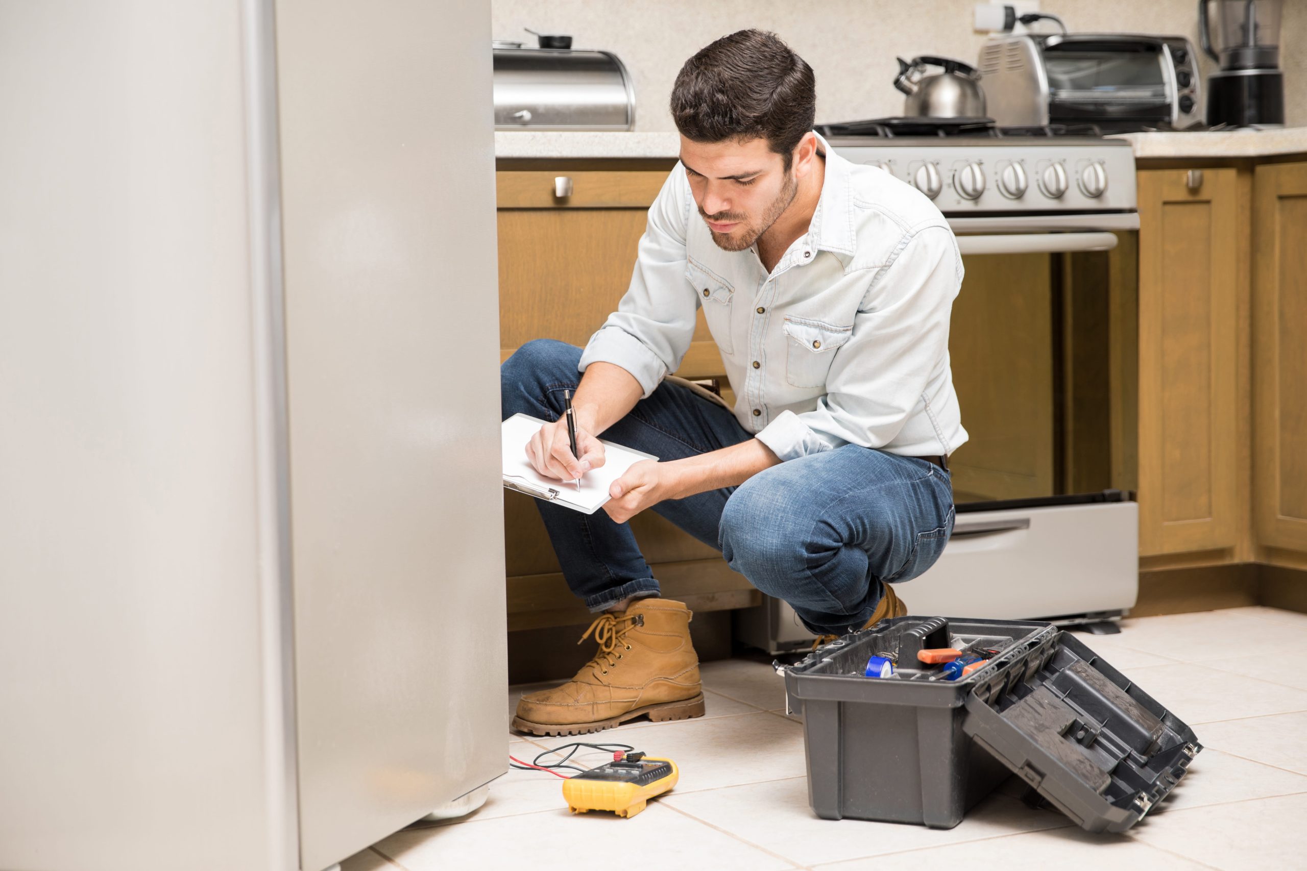 portrait-handsome-male-technician-doing-work-report-broken-fridge-home-kitchen (1)